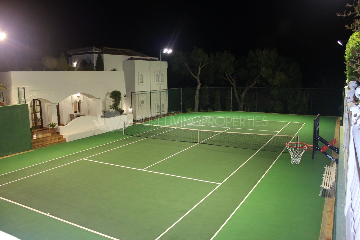 There is an outdoor tennis court with a basketball hoop